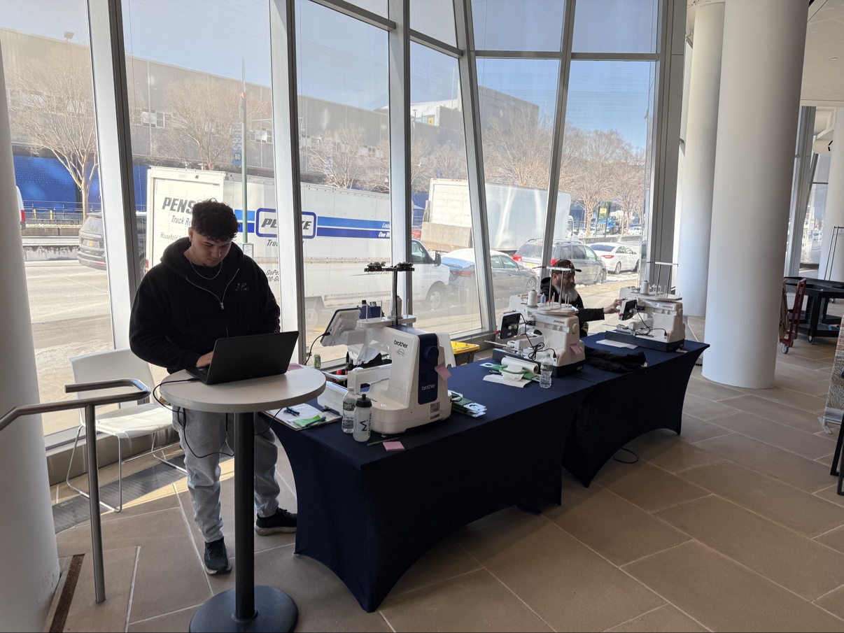 Three embroidery machines set up on a draped event table in a bright venue lobby, with the crew at the check-in laptop
